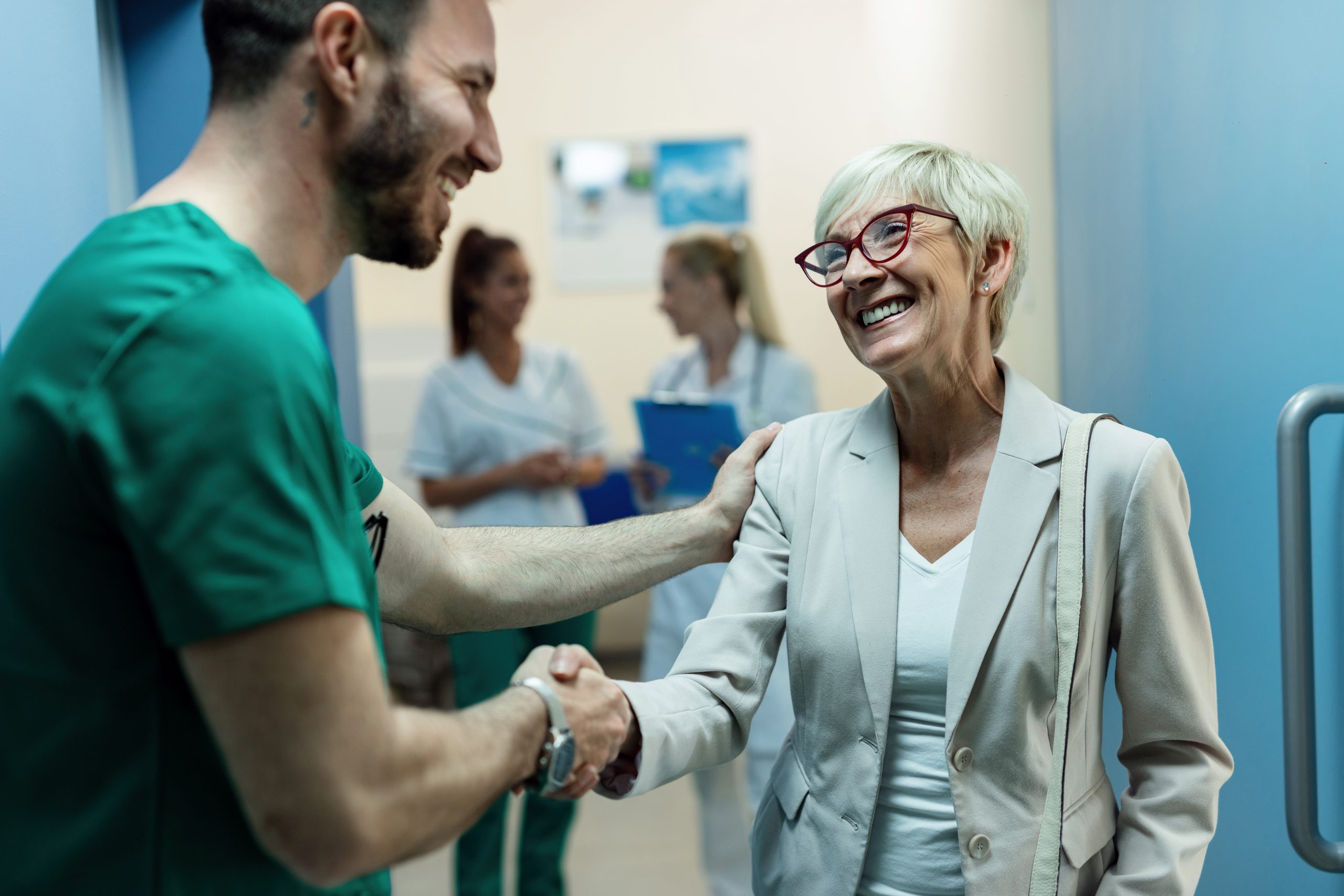 Happy senior woman shaking hands with a surgeon at hospital hallway.