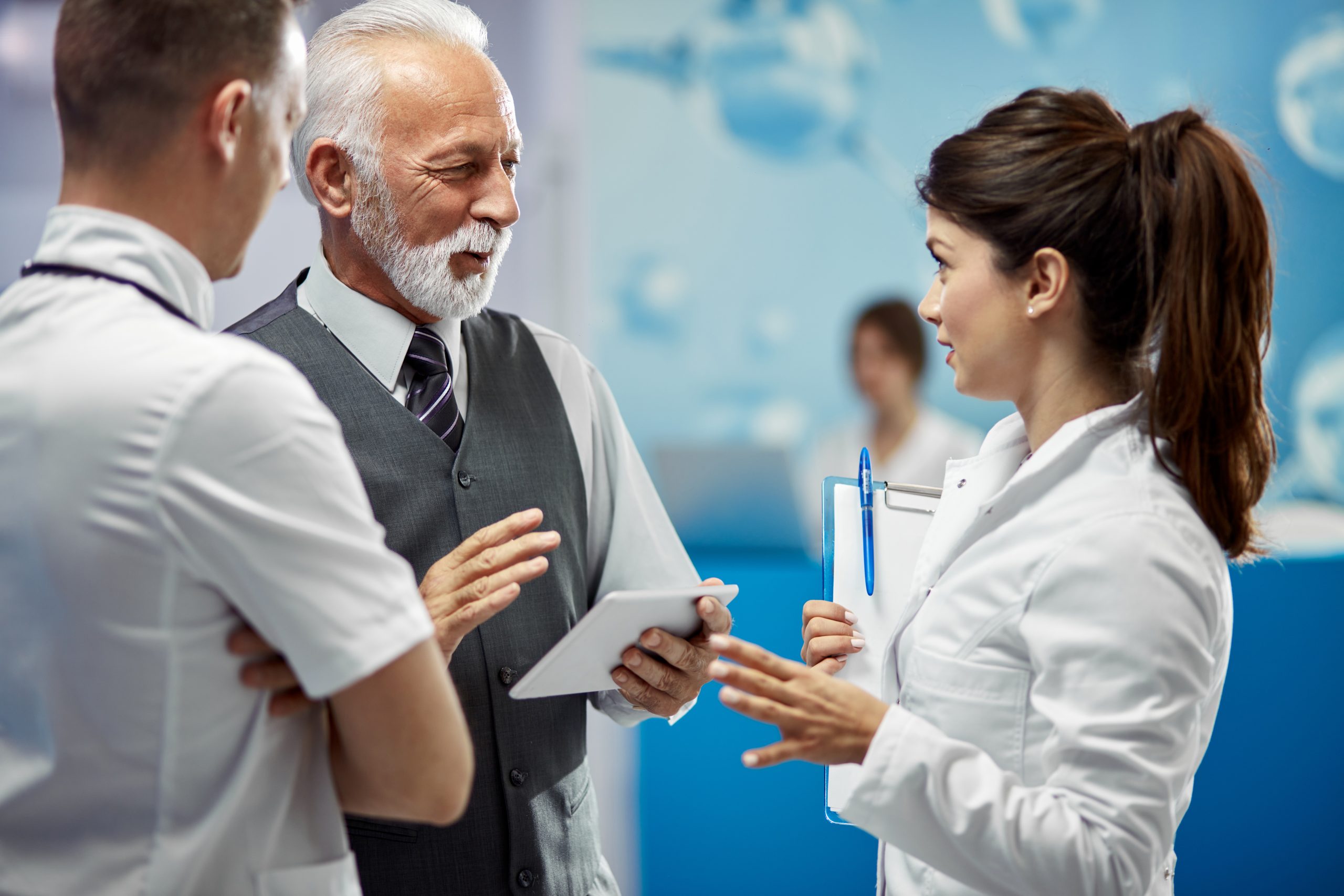 Happy senior businessman talking to doctors in hallway at the hospital